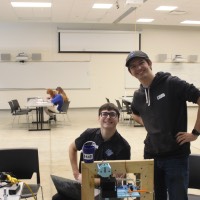 Two students standing next to a third block elevator project.